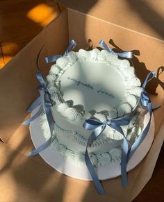 a white cake with blue ribbons in a box