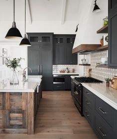 a large kitchen with black cabinets and white counter tops, wooden flooring and hanging lights