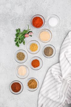 spices and seasonings arranged in bowls on a white surface with a towel next to them