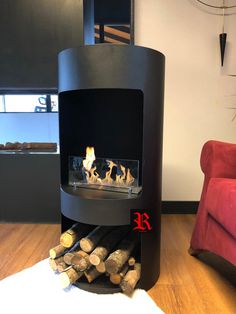 a fire place in the middle of a living room with logs on the floor and a red chair