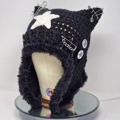 a knitted hat with buttons and chains on it sitting on a glass plate in front of a white background