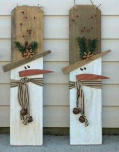 three snowmen made out of wooden boards on the side of a building with pine cones