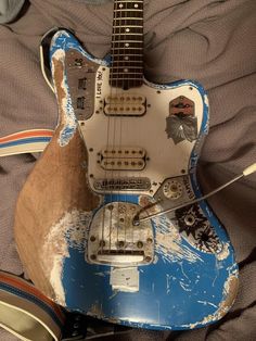 an old blue and white guitar sitting on top of a bed