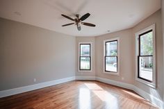 an empty room with three windows and a ceiling fan