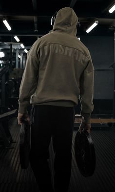 a man in a hoodie carrying two dumbbells