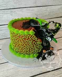 a cake decorated with green and black icing on a white plate next to a dirt bike