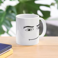 a white coffee mug with a face drawn on the inside of it sitting on a table next to a book