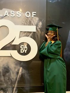 a woman in a graduation gown talking on her cell phone while standing next to a sign