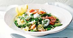 a white bowl filled with pasta and vegetables on top of a table next to silverware