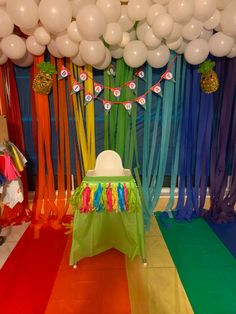 a rainbow themed birthday party with balloons and streamers on the ceiling, table cloths draped over it