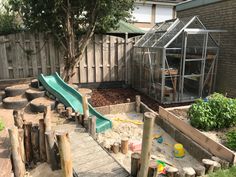 an outdoor play area with a slide, sandbox and tree stumps in the foreground