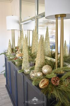 christmas decorations on top of a buffet with pine cones and gold balls in the center