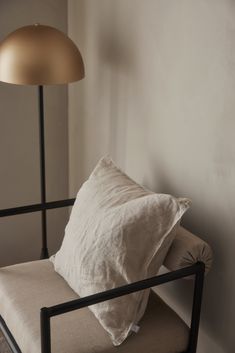 a white pillow sitting on top of a brown chair next to a lamp and wall