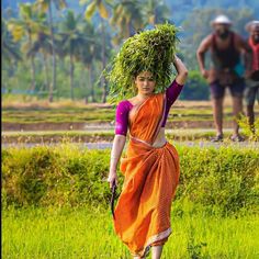 a woman walking in the grass carrying plants on her head with two men behind her