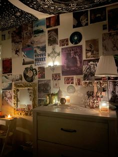 a room filled with lots of pictures on the wall next to a dresser and lamp