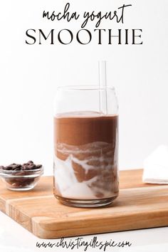 a glass filled with chocolate smoothie sitting on top of a wooden cutting board