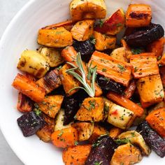 a white bowl filled with roasted carrots and potatoes