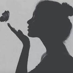 the silhouette of a woman holding a butterfly in one hand and looking at it in the other