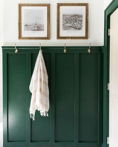 two framed pictures hang on the wall next to a green coat rack in a bathroom