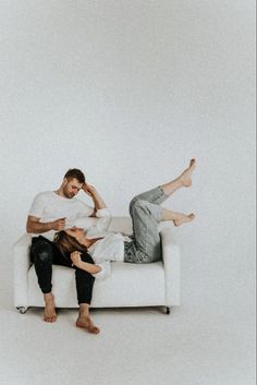 two people sitting on a white couch with their feet up against the back of each other