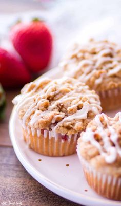 some muffins are sitting on a plate with strawberries in the back ground