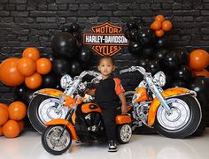 a young boy is sitting on an orange motorcycle in front of balloons and black balls