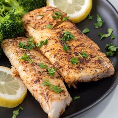 two pieces of fish on a plate with broccoli and lemon