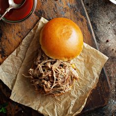 a pulled pork sandwich sitting on top of a wooden cutting board next to a cup of tea