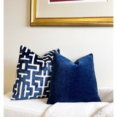 two blue and white pillows sitting on top of a couch next to a framed painting