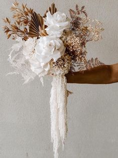 a person holding a bouquet of flowers in their hand with white and brown foliage on it