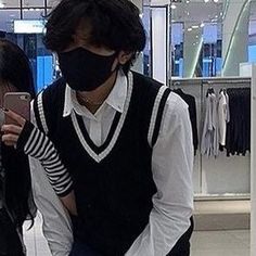 a man and woman wearing face masks while looking at their cell phones in a clothing store