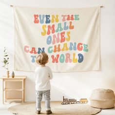 a little boy standing in front of a wall hanging with the words even the small ones can change the world