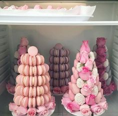 pink and purple macaroons are arranged on white plates in a refrigerator with flowers