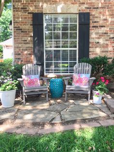 two chairs sitting in front of a window on top of a stone patio next to potted plants