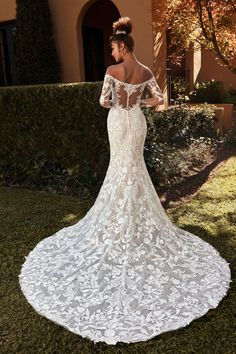 a woman in a white wedding dress standing on the grass with her back to the camera