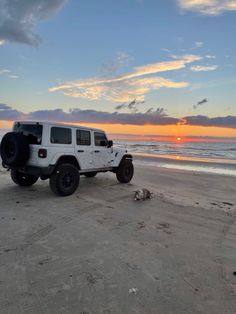 a white jeep parked on top of a sandy beach next to the ocean at sunset