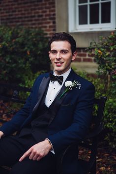 a young man in a tuxedo sitting on a bench wearing a boutonniere