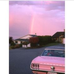 a pink car is parked in front of a house with a rainbow in the background