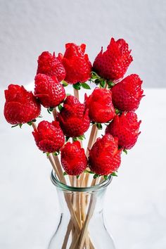 a glass vase filled with strawberries on top of a white tablecloth and wooden sticks