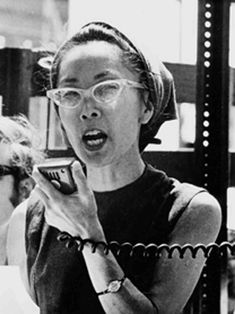 a woman wearing glasses talking on a cell phone while standing in front of a mirror