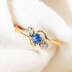 a gold ring with three blue and white stones on it, sitting on a white cloth