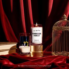 a candle next to a birdcage on a red cloth with the words forbidden forest printed on it