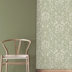 a chair sitting in front of a wall with a green floral pattern on the wall