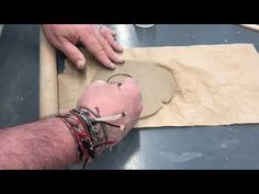 a man is making something out of clay with his hands on the edge of a piece of paper