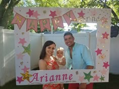 a man and woman holding a baby in front of a happy birthday sign with stars on it