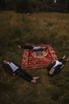 two people laying on a rug in the middle of a field with their arms around each other