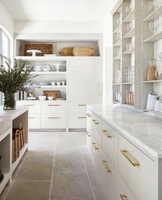 a kitchen with white cabinets and gold pulls on the doors, shelves filled with dishes