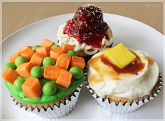 three cupcakes on a white plate topped with frosting and fruit toppings