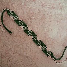 a green and white beaded tie laying on top of a pink blanket