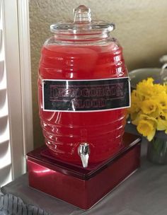 a large red beverage dispenser sitting on top of a table next to yellow flowers